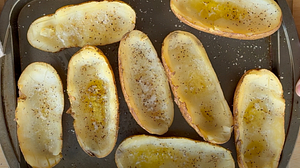 Half-scooped potato skins brushed with olive oil and seasoned with salt and pepper, ready for grilling on a tray.