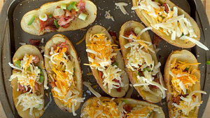 Stuffed potato skins loaded with bacon, green onions, and mixed cheese on a baking tray, prepped for grilling