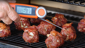 Checking the internal temperature of bacon-wrapped meatballs on a Z Grills pellet grill, thermometer reading 167°F.