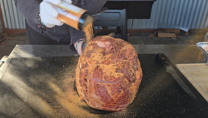 Applying a savory rub to a spiral ham, enhancing its flavors before grilling.