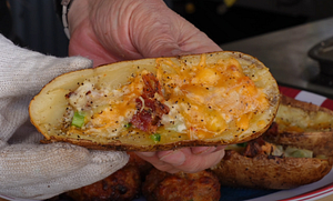 Close-up view of a hand holding a loaded potato skin filled with melted cheddar cheese, bacon bits, and green onions, cooked on a Z Grills pellet grill.