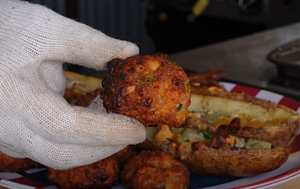 Close-up of a smoked sausage ball held in a gloved hand, with loaded potato skins in the background, prepared on a Z Grills pellet grill.