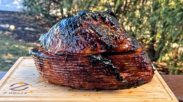 Glazed ham beautifully caramelized, presented on a wooden cutting board set against a natural outdoor backdrop.